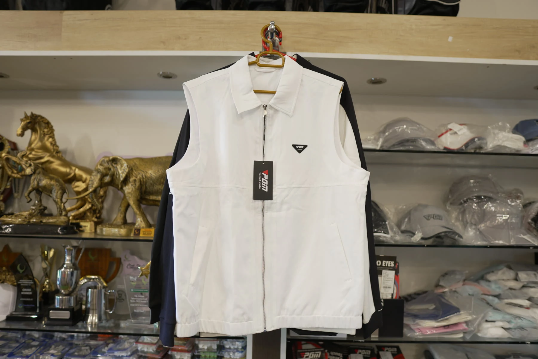 A white sleeveless Callaway golf vest on a hanger in front of trophy shelves