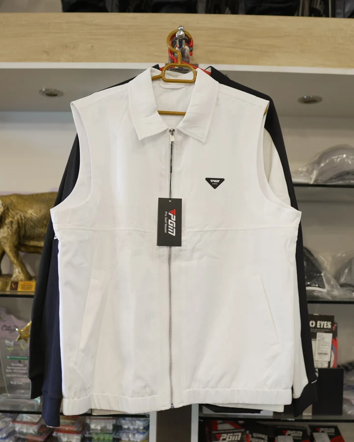 A white sleeveless Callaway golf vest on a hanger in front of trophy shelves