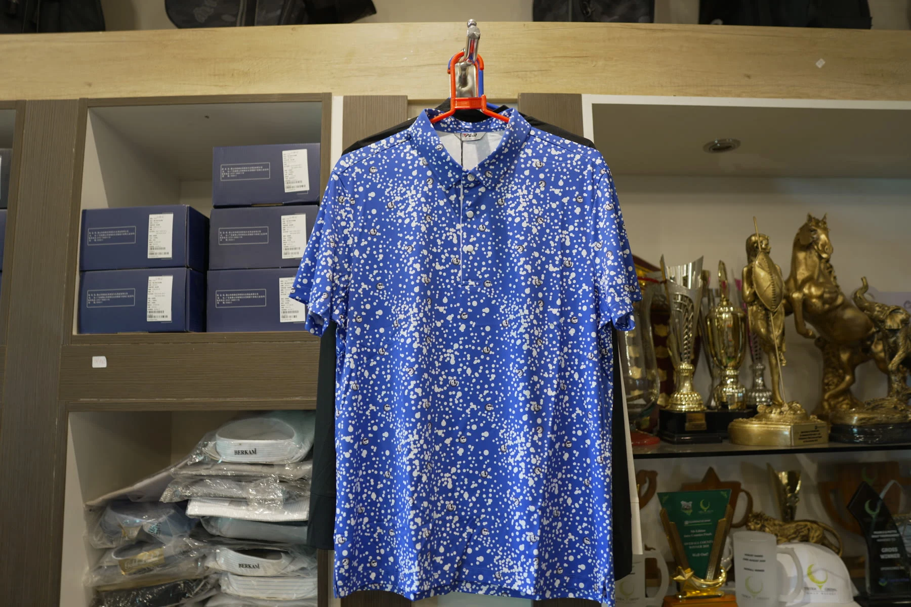 A blue patterned golf polo shirt on a hanger against the shop's shelving