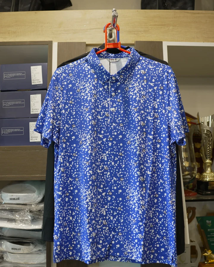 A blue patterned golf polo shirt on a hanger against the shop's shelving