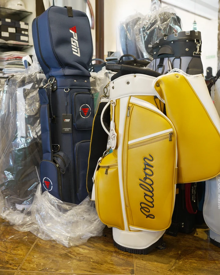 A navy PGM staff bag with a red logo standing on the pro shop floor