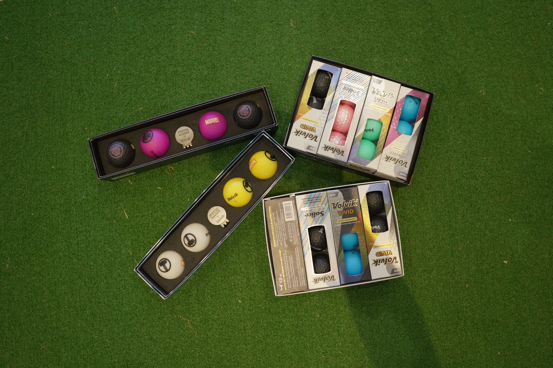 Boxes of white, yellow and pink golf balls displayed on putting turf