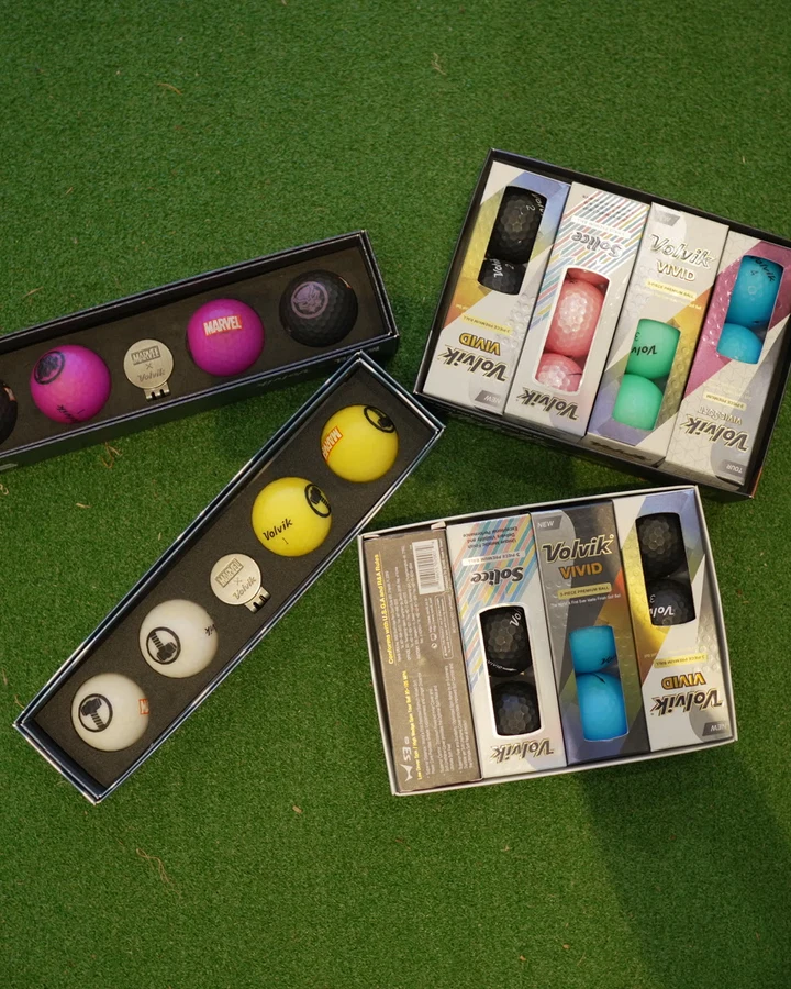 Boxes of white, yellow and pink golf balls displayed on putting turf