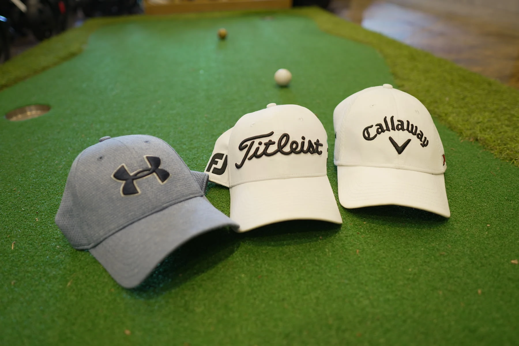Titleist, Callaway and Under Armour caps arranged on the shop's putting turf