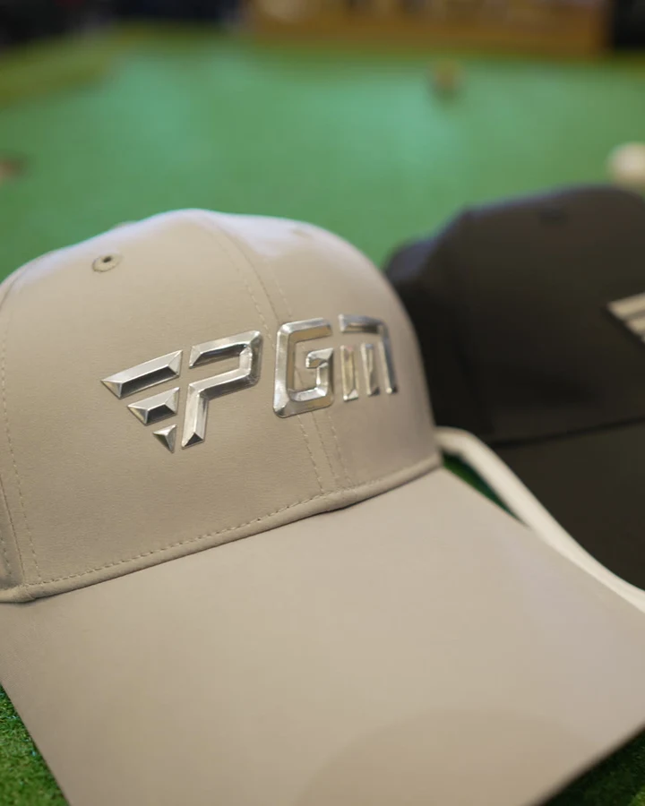 Three PGM golf caps in stone, black and white arranged on putting turf
