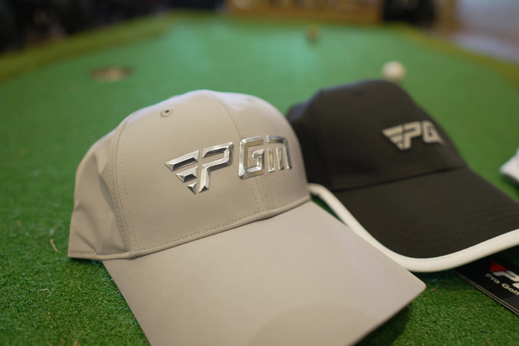 Three PGM golf caps in stone, black and white arranged on putting turf