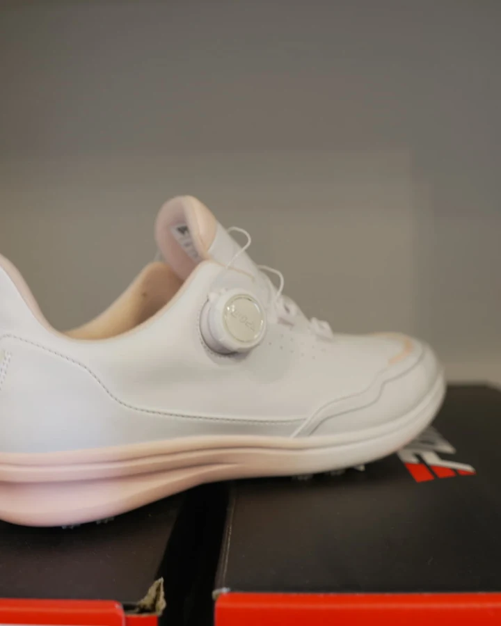 A white golf shoe with a dial closure system displayed on its box