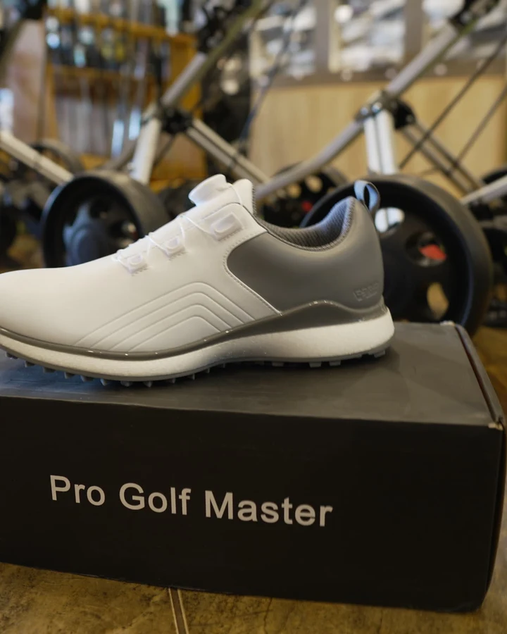 A grey and white spikeless golf shoe displayed on a Pro Golf Master box