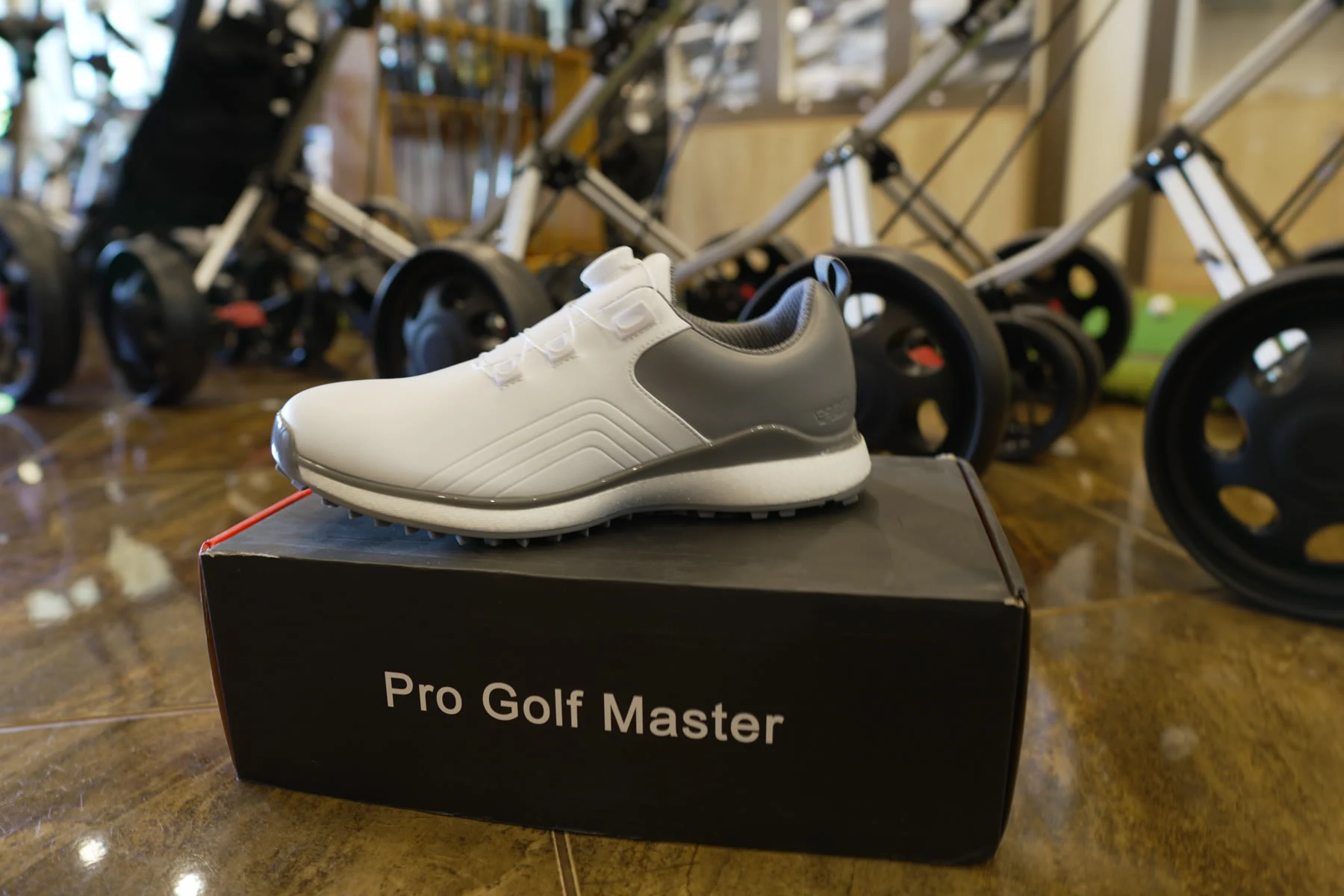 A grey and white spikeless golf shoe displayed on a Pro Golf Master box