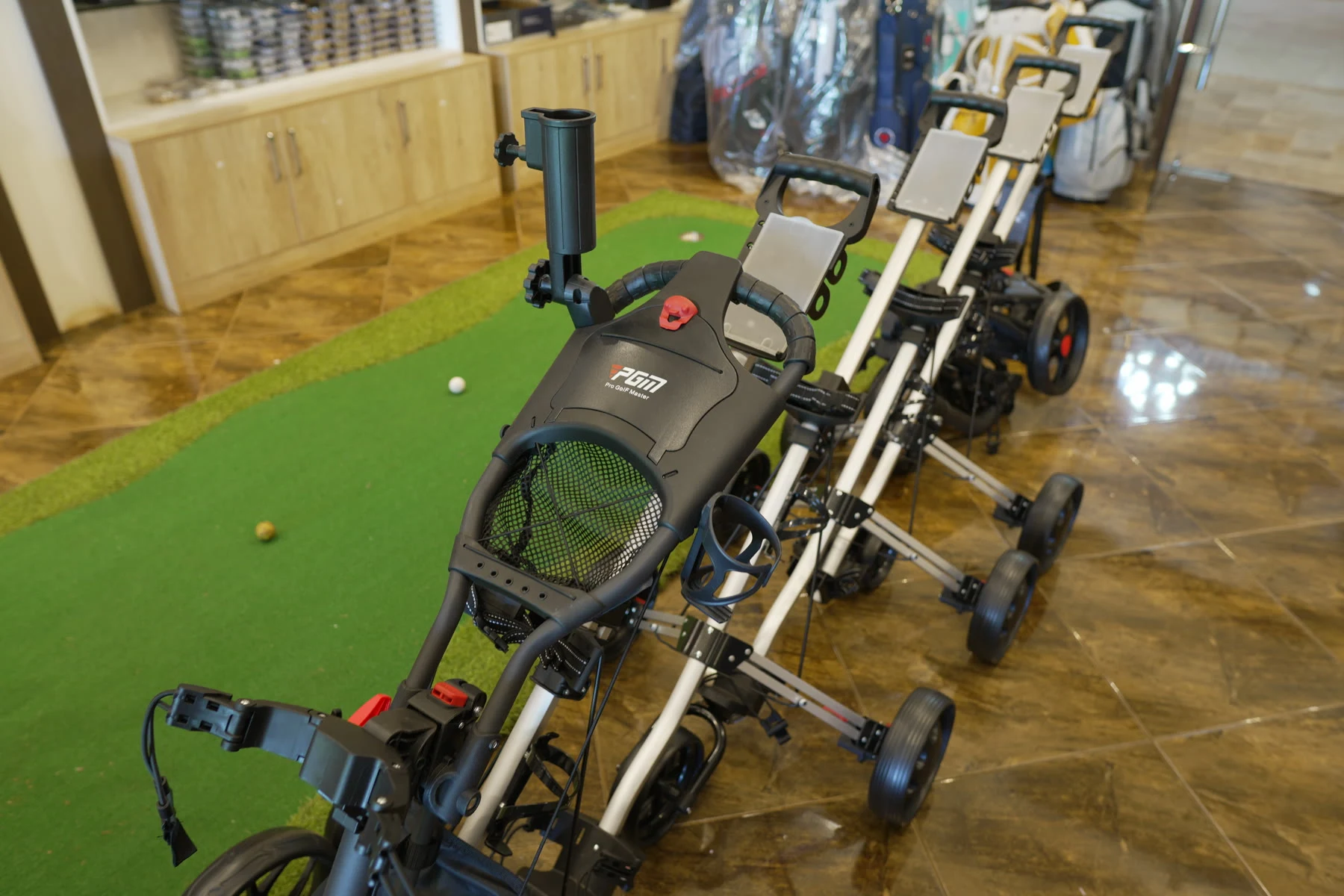 Folded and upright PGM push trolleys lined up on the shop's putting turf